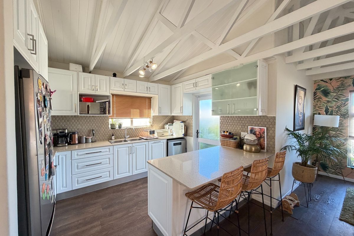 Modern kitchen featuring white shaker cabinetry, stone countertops, a central island with breakfast bar seating, and distinctive exposed timber ceiling beams.