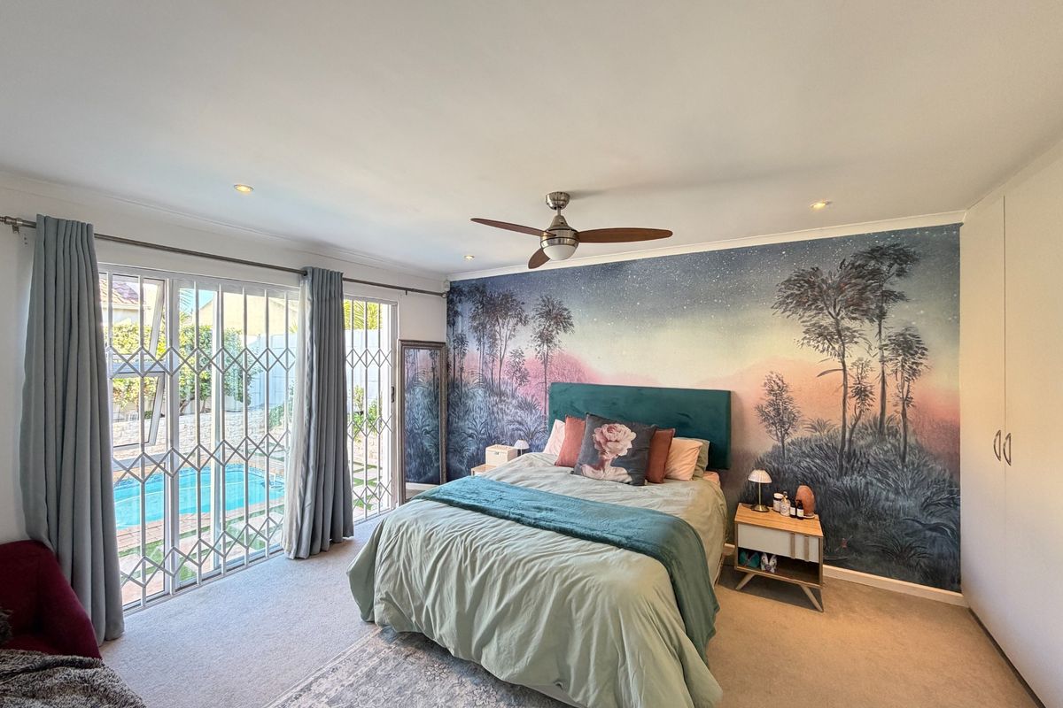 Spacious bedroom featuring a decorative mural wall, ceiling fan, built-in cupboards, and sliding glass doors providing direct access to the pool area.