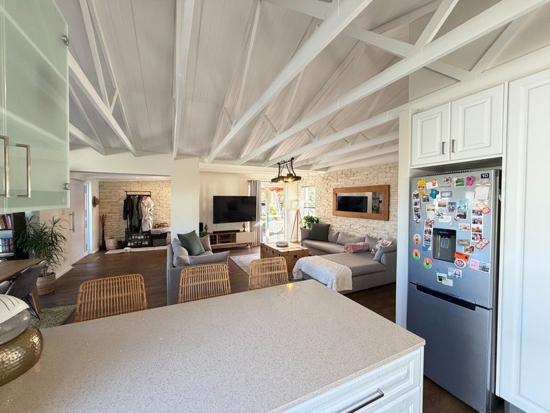 Spacious open-plan living area featuring a high exposed beam ceiling, stone feature walls, and a modern kitchen with a central island.