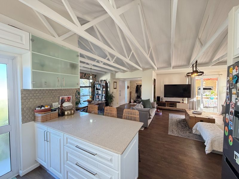 Spacious open-plan living area featuring a modern kitchen with stone countertops, vaulted ceilings with exposed trusses, and seamless flow to the outdoor patio.