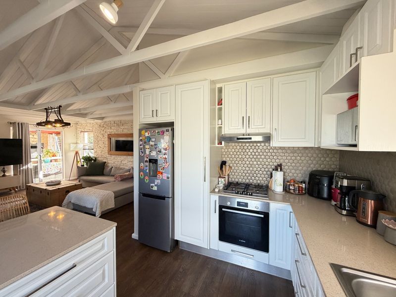 Open-plan kitchen and living area featuring exposed vaulted ceilings, stone feature wall, modern cabinetry, and high-quality stone countertops with integrated appliances.