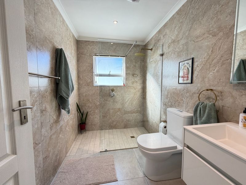 Modern bathroom featuring floor-to-ceiling stone-look tiles, a spacious walk-in shower with a rain shower head, and a sleek vanity unit.
