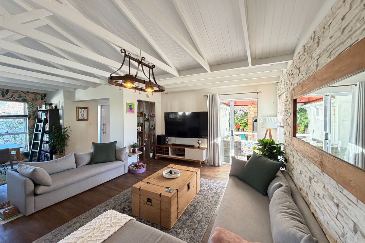 Spacious living room featuring a vaulted timber beam ceiling, a textured stone feature wall, and direct access to an outdoor patio area.