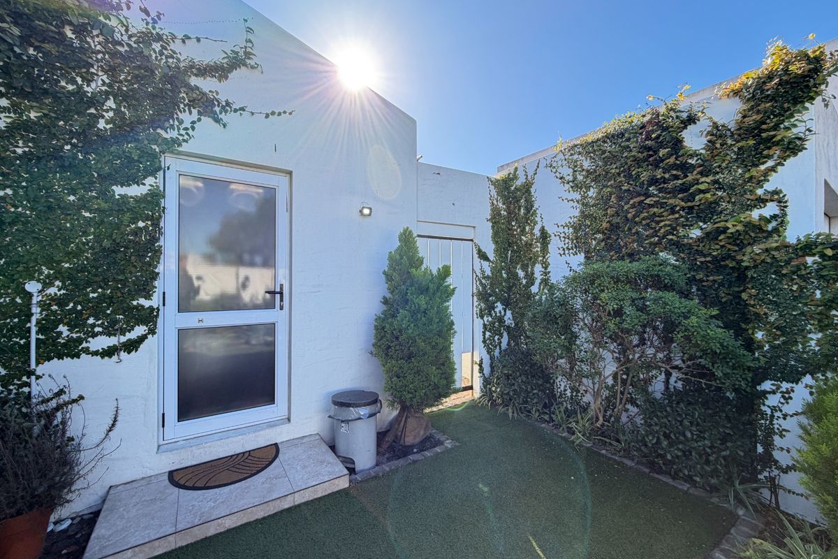 A private rear courtyard area featuring artificial turf, climbing ivy on the walls, and a tiled entrance step leading to a glass panel door.