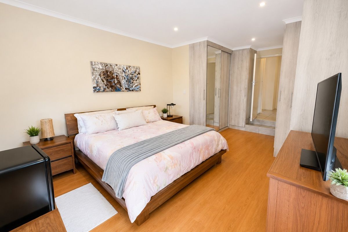A well-maintained bedroom featuring laminate flooring, built-in cupboards with mirrored doors, and recessed downlighting.