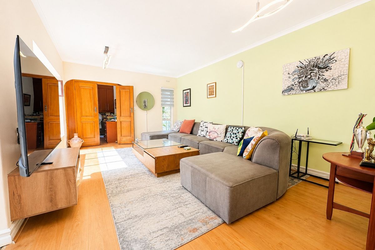 A bright and spacious living room featuring laminate flooring, coved ceilings, and double wooden doors leading to an adjacent room.