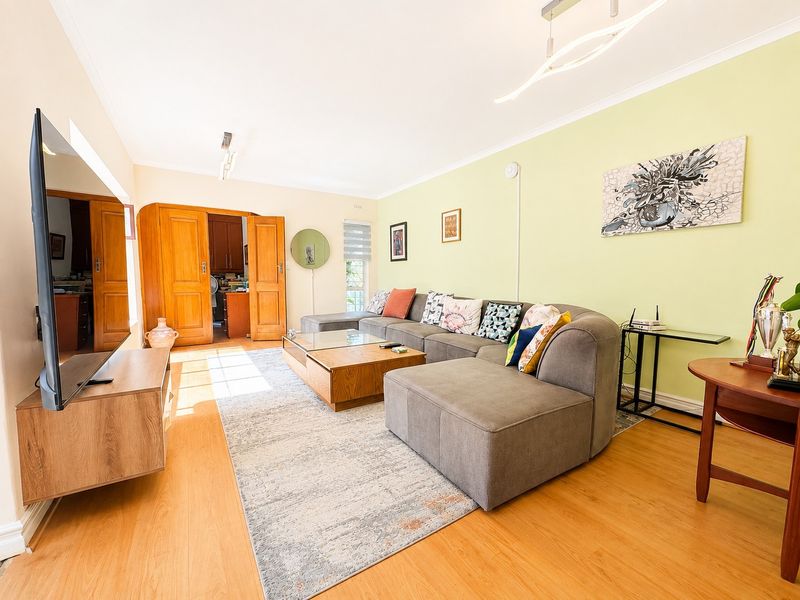 A bright and spacious living room featuring laminate flooring, coved ceilings, and double wooden doors leading to an adjacent room.