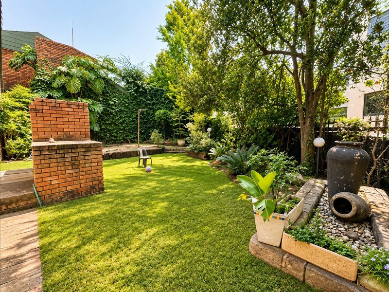 A well-maintained private garden featuring a brick braai, established trees, and a decorative stone water feature.