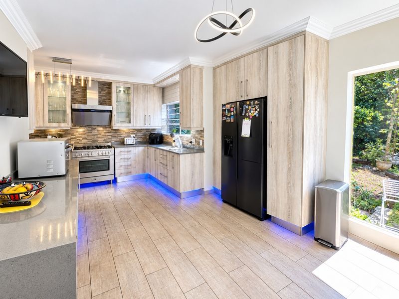 Modern kitchen featuring light wood-grain cabinetry, stone countertops, gas stove with extractor, and integrated under-cabinet lighting, overlooking a private garden.