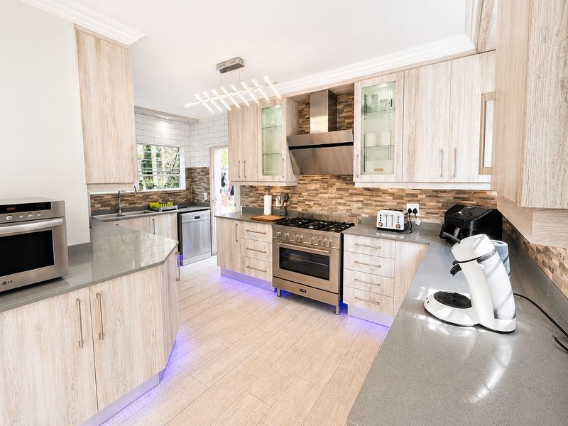 Modern kitchen featuring light wood cabinetry, stone countertops, gas stove with extractor fan, and stylish under-cabinet lighting.