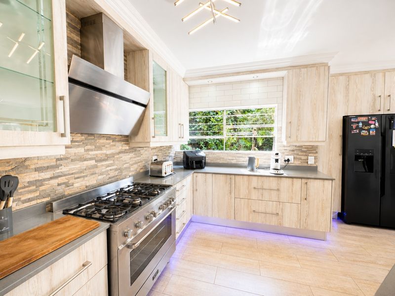 Modern kitchen featuring light wood cabinetry, stone veneer and subway tile backsplashes, stainless steel gas stove, and integrated under-cabinet lighting.