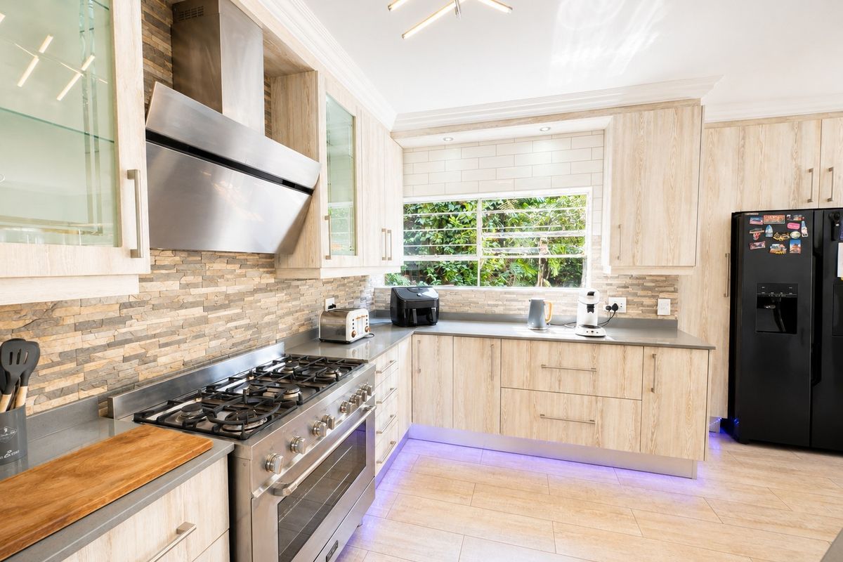Modern kitchen featuring light wood cabinetry, stone veneer and subway tile backsplashes, stainless steel gas stove, and integrated under-cabinet lighting.