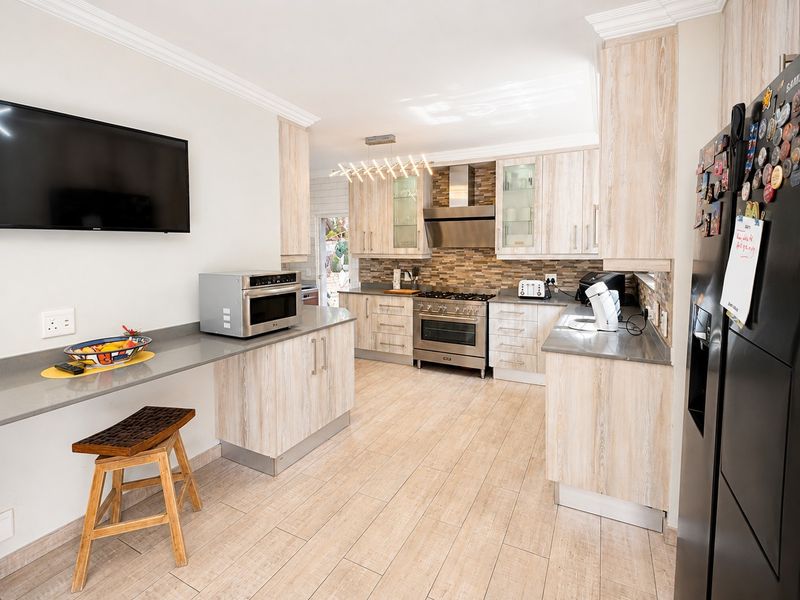 Modern kitchen featuring light wood-grain cabinetry, stone countertops, stainless steel gas range, and tiled backsplash with integrated breakfast bar area.