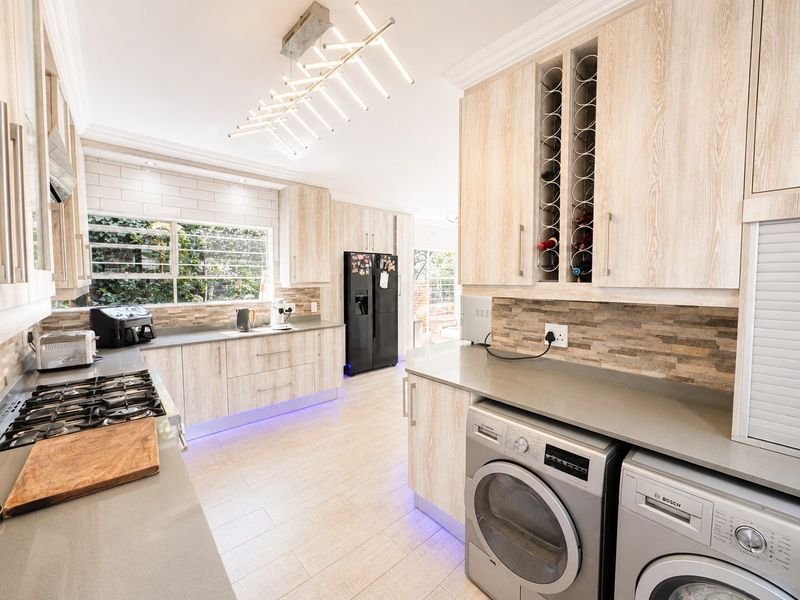 Modern kitchen featuring light wood cabinetry, stone countertops, integrated appliances, gas cooktop, and stylish under-cabinet lighting.