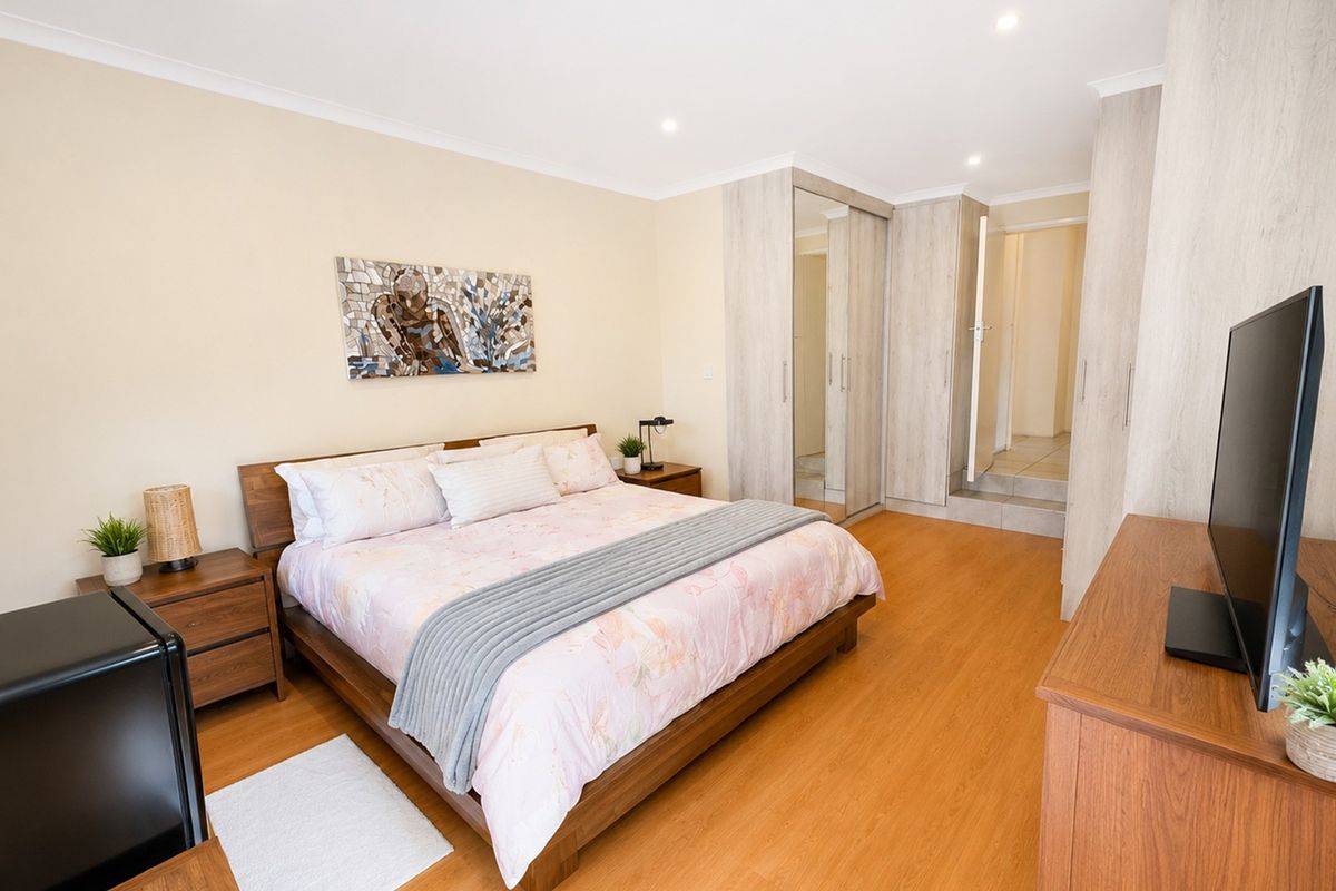 A well-maintained bedroom featuring laminate flooring, built-in cupboards with mirrored panels, and recessed ceiling lighting.