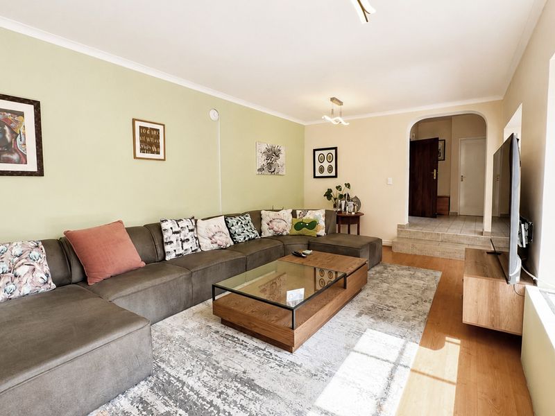 A comfortable living room featuring laminate flooring, a coved ceiling, and an arched entryway leading to the rest of the home.