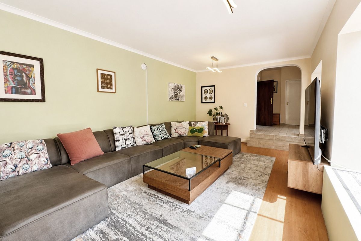 A comfortable living room featuring laminate flooring, a coved ceiling, and an arched entryway leading to the rest of the home.