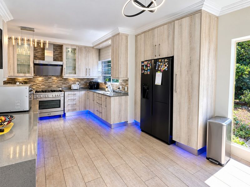 Modern kitchen featuring light wood cabinetry, stone countertops, gas stove with extractor, and integrated under-cabinet lighting, with direct access to the garden.