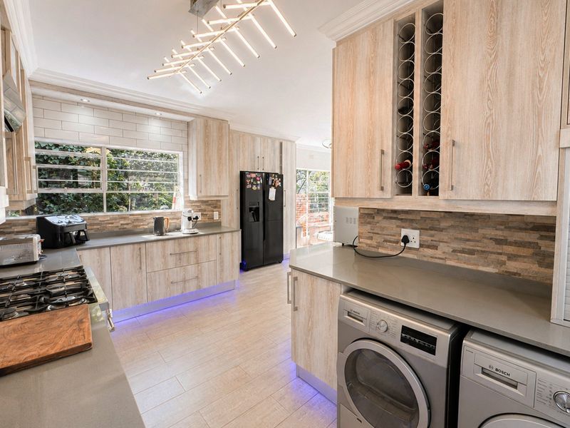 Modern kitchen featuring light wood cabinetry, stone countertops, gas hob, integrated wine rack, and stylish under-cabinet lighting with tiled flooring.