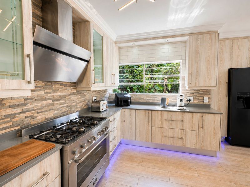 Modern kitchen featuring light wood cabinetry, stone veneer backsplash, gas stove with extractor fan, and integrated under-cabinet lighting.