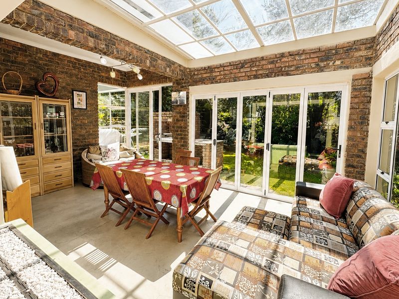 Spacious sunroom featuring exposed brick walls, a glass roof, and bi-fold doors that open onto the garden, creating a bright, versatile living space.
