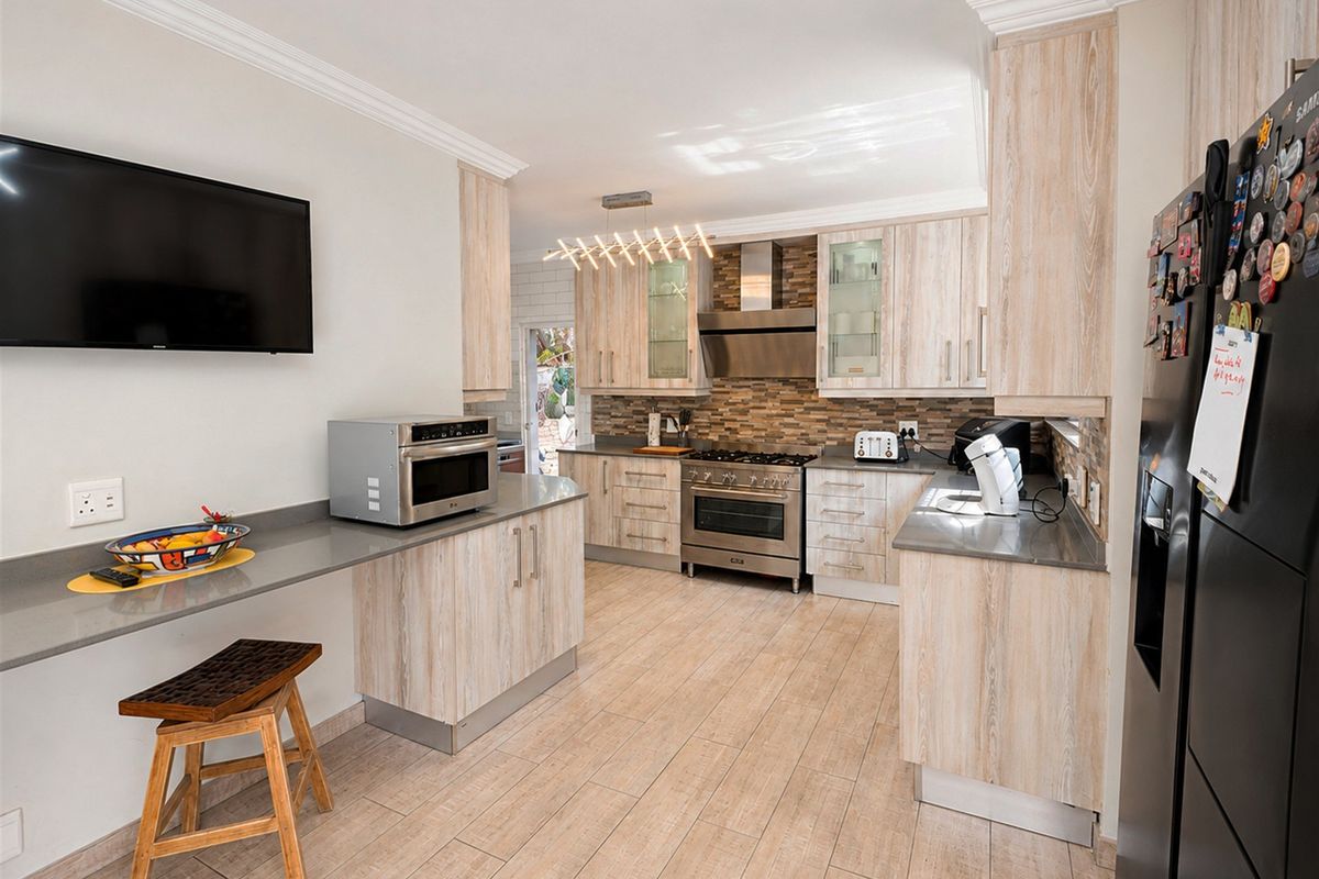 Modern kitchen featuring light wood-grain cabinetry, stone countertops, a gas stove with extractor fan, and tiled flooring with a breakfast bar area.