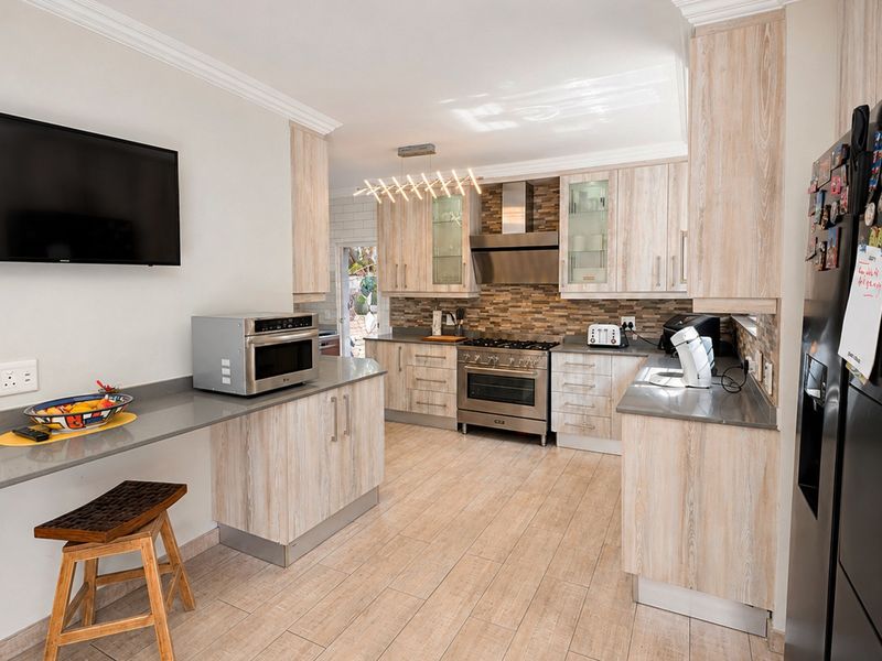 Modern kitchen featuring light wood-grain cabinetry, stone countertops, a gas stove with extractor fan, and tiled flooring with a breakfast bar area.