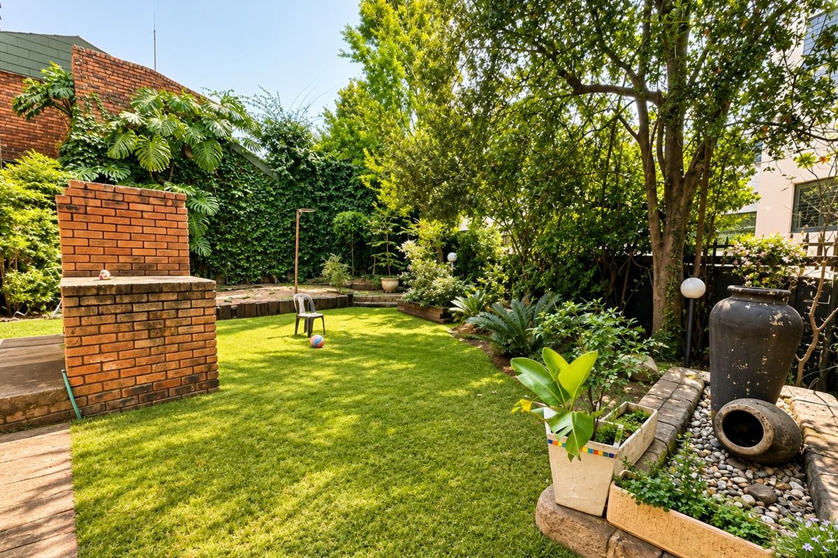 A private rear garden featuring a brick built-in braai, lush lawn, mature trees, and a decorative stone water feature.