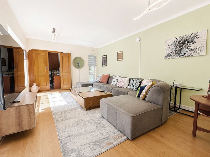 Spacious living room featuring light laminate flooring, neutral walls, and double timber doors leading to an adjacent room.