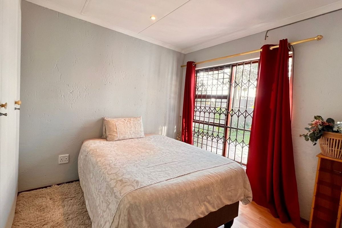 A functional bedroom featuring built-in cupboards, laminate flooring, and a sliding door with security gate providing access to the exterior.