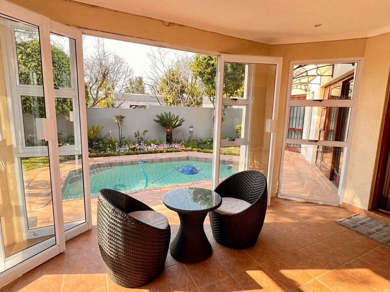 A covered patio area featuring tiled flooring and large aluminium sliding doors that open directly onto a private swimming pool and garden area.