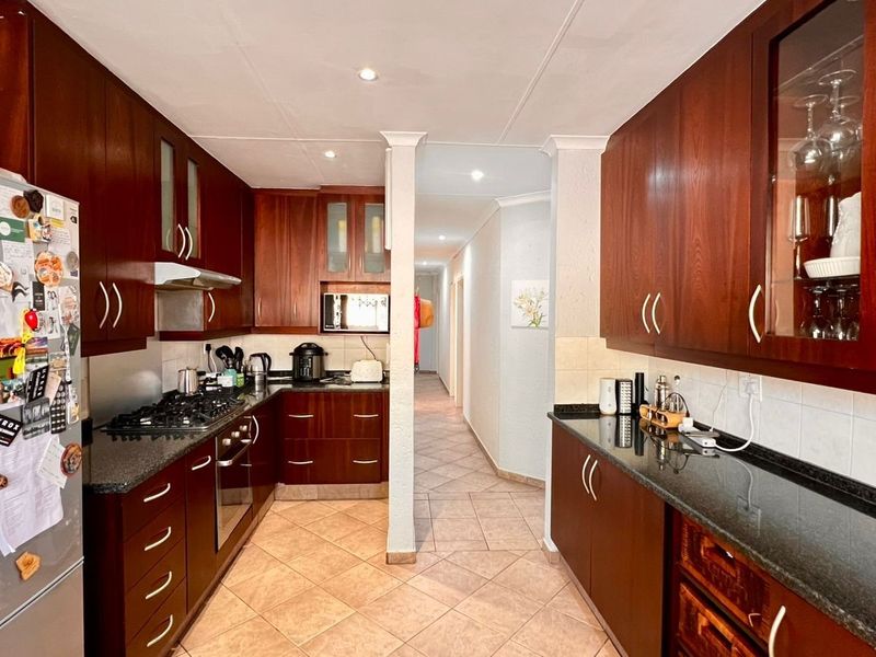 A functional kitchen featuring dark wood cabinetry, granite countertops, a gas hob, and tiled flooring, leading into a hallway.
