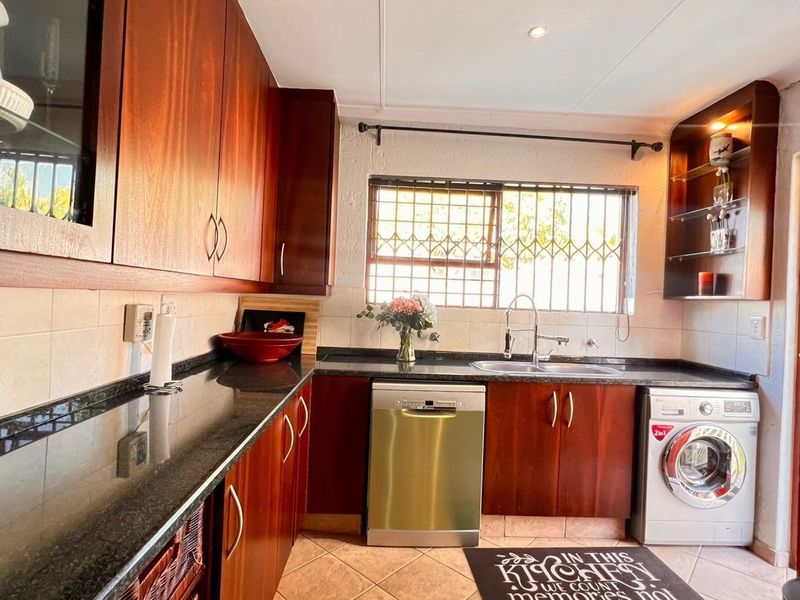 A functional kitchen featuring dark wood cabinetry, granite countertops, tiled flooring, and integrated appliances including a dishwasher and washing machine.