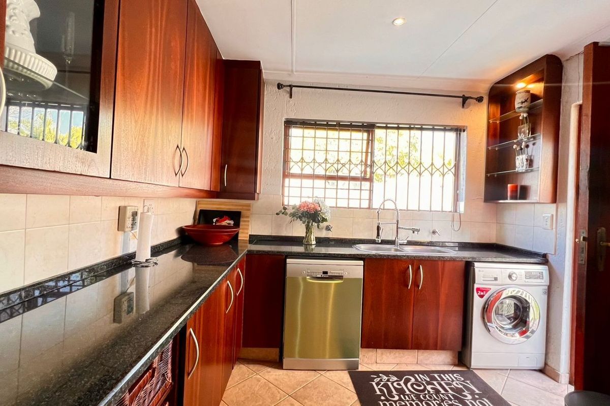 A functional kitchen featuring dark wood cabinetry, granite countertops, tiled flooring, and integrated appliances including a dishwasher and washing machine.