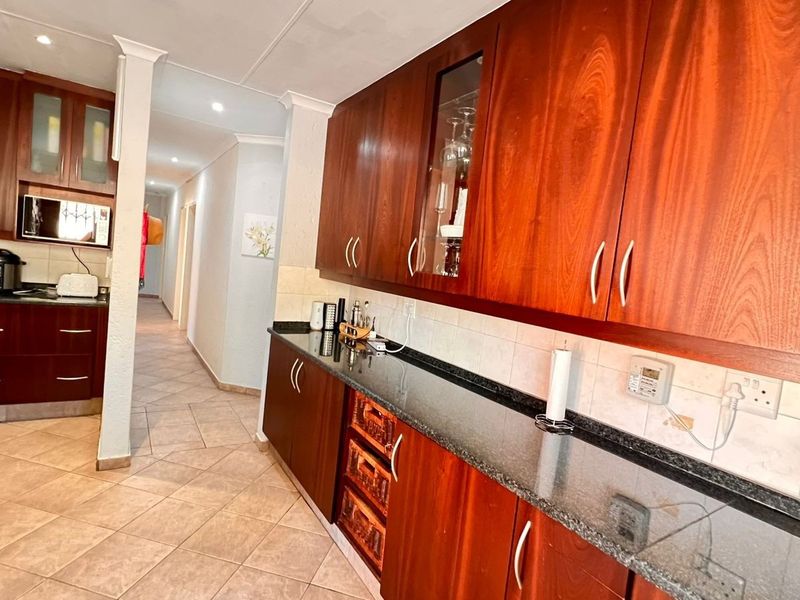 A functional kitchen featuring dark wood cabinetry, granite countertops, tiled flooring, and integrated appliances, leading into a hallway.
