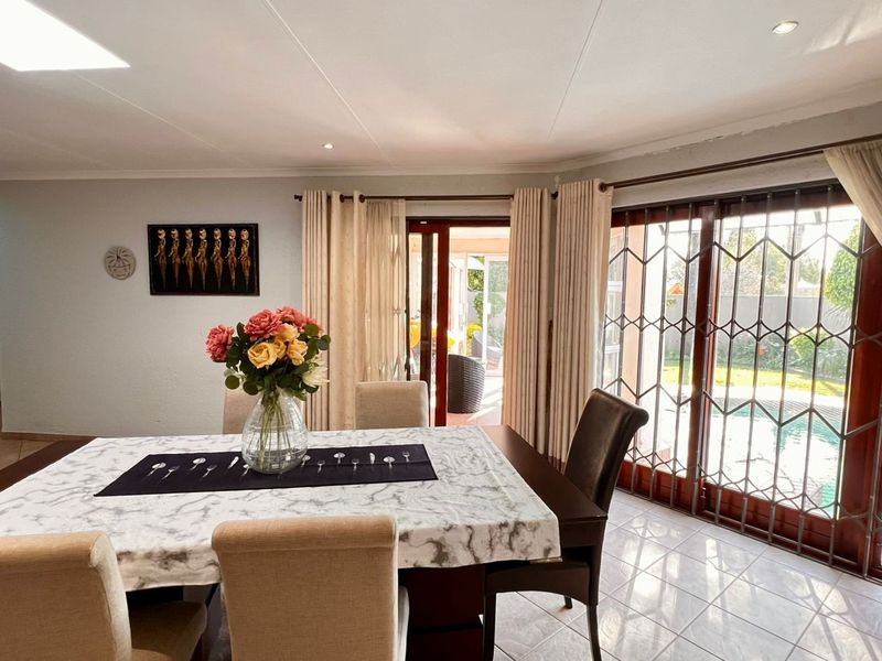 A bright dining room featuring tiled flooring and large sliding glass doors with security gates, providing direct access to the outdoor pool area.