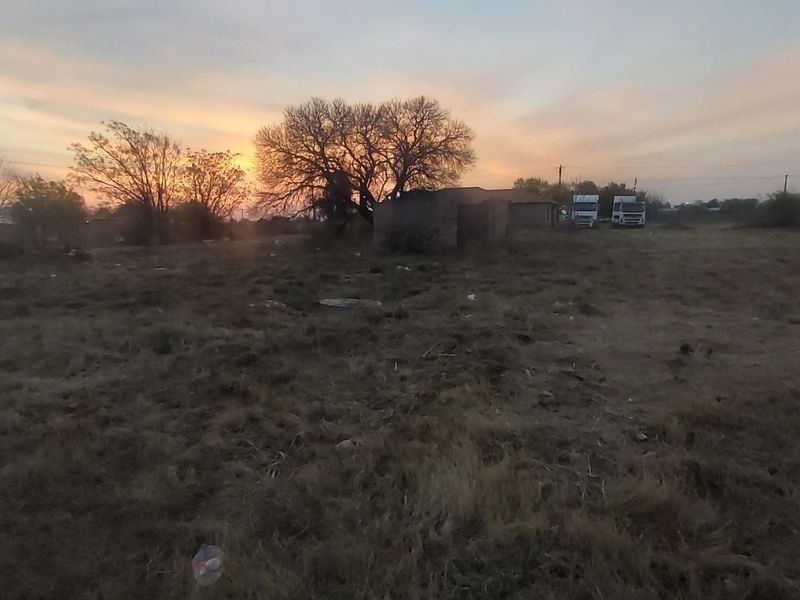 A vacant residential plot featuring open land, boundary walling, and utility infrastructure at sunset.