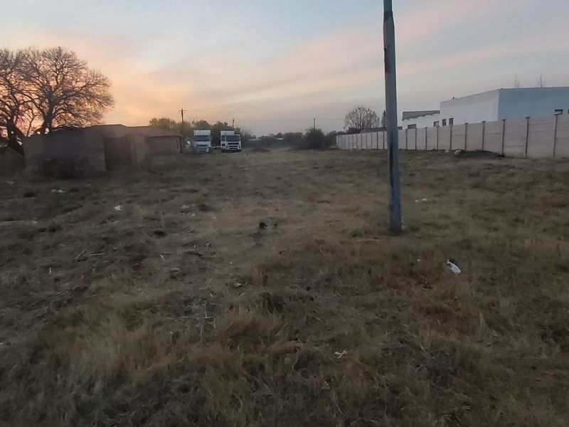 A vacant residential plot featuring a precast concrete boundary wall and utility pole, captured during sunset.