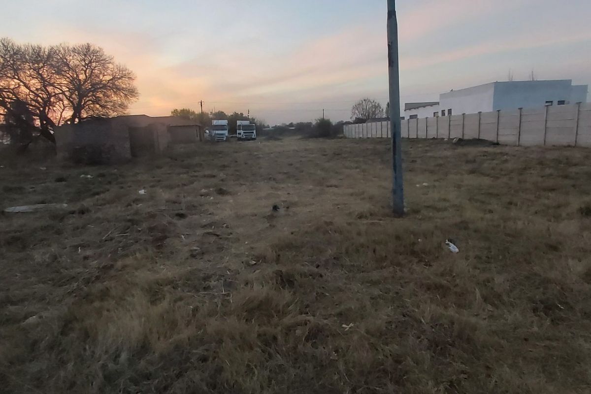 A vacant residential plot featuring a precast concrete boundary wall and utility pole, captured during sunset.
