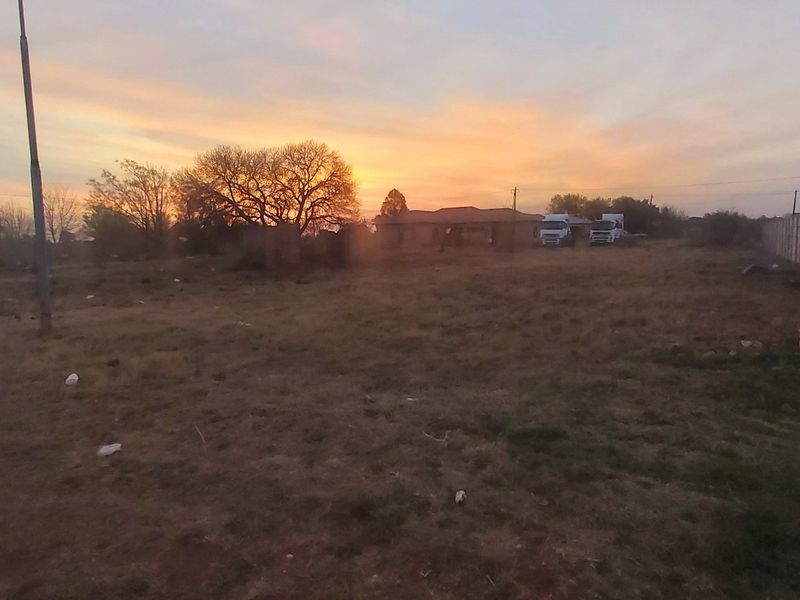 A vacant residential plot featuring a precast concrete boundary wall and open land, captured during sunset.