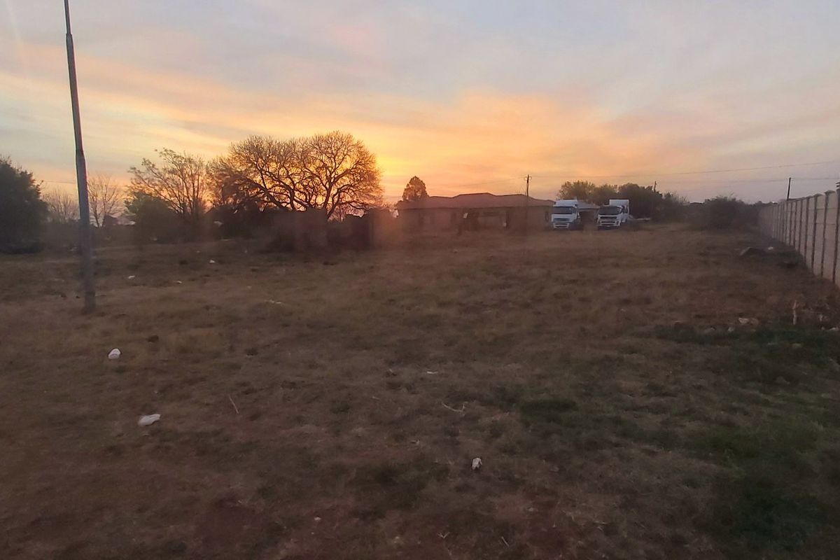 A vacant residential plot featuring a precast concrete boundary wall and open land, captured during sunset.