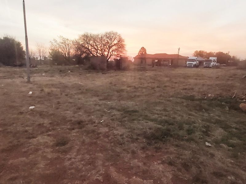 A wide-angle view of a vacant residential plot featuring dry grass, perimeter fencing, and a utility pole at sunset.
