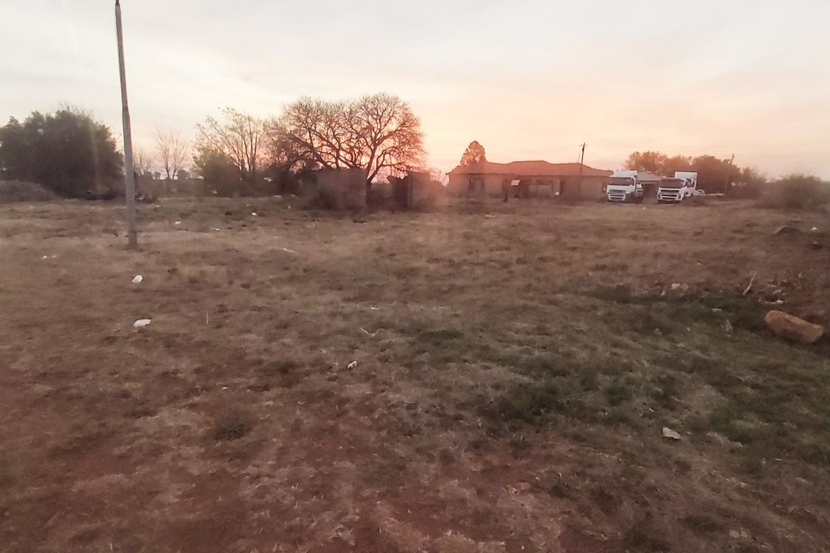 A wide-angle view of a vacant residential plot featuring dry grass, perimeter fencing, and a utility pole at sunset.