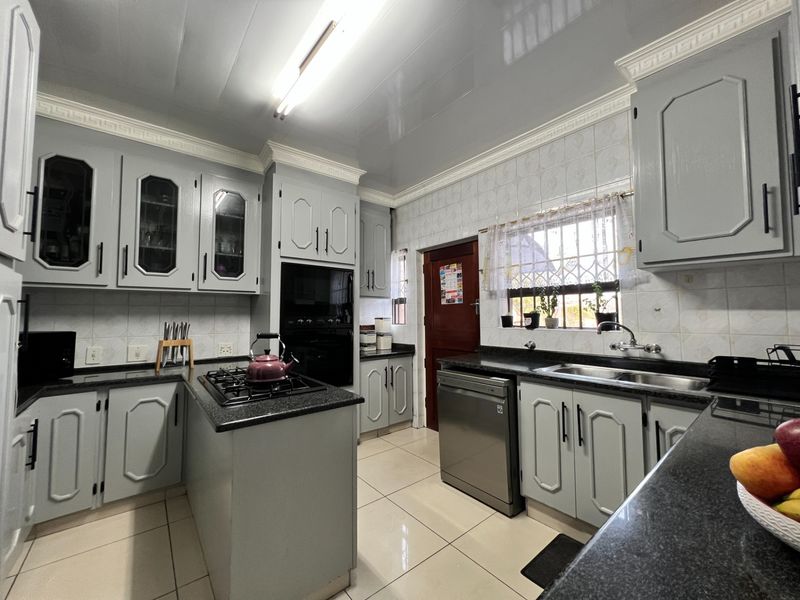 A well-maintained kitchen featuring grey cabinetry, granite countertops, a gas hob, built-in oven, and tiled flooring with a functional layout.