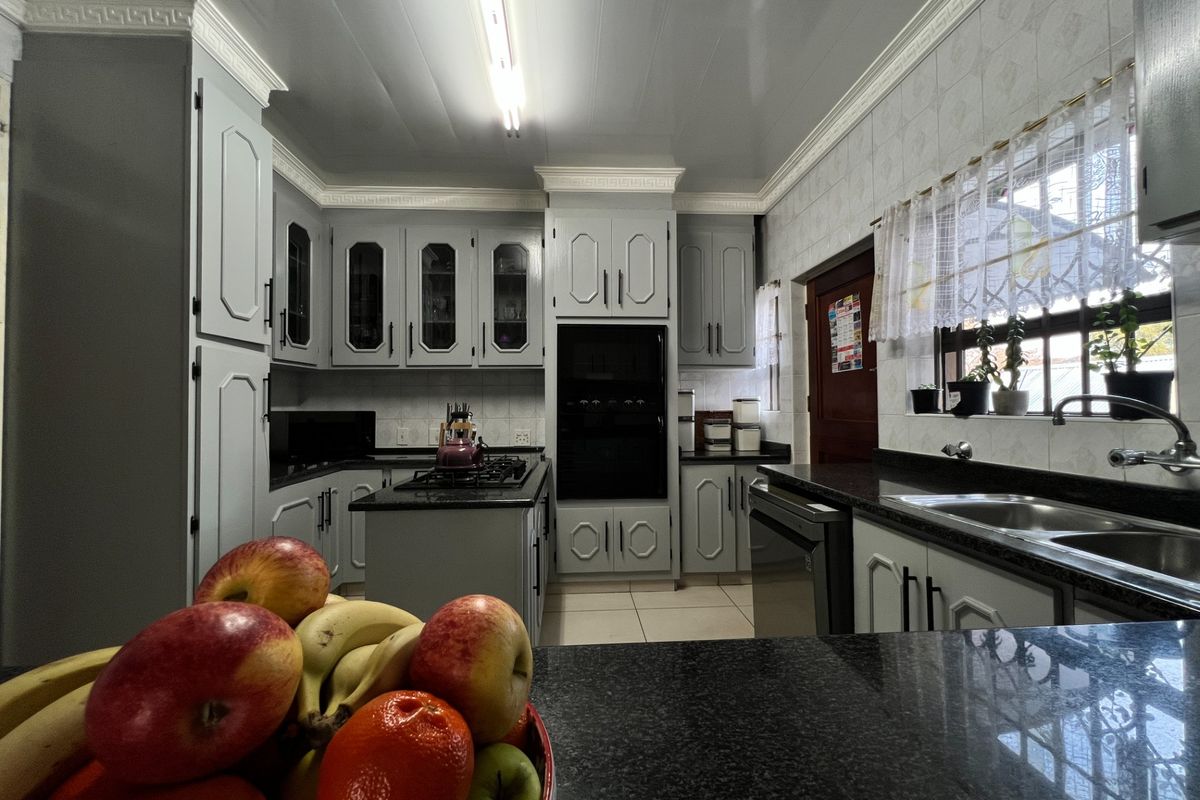 A well-maintained kitchen featuring grey cabinetry, granite countertops, a gas hob, and a built-in oven with classic crown molding details.