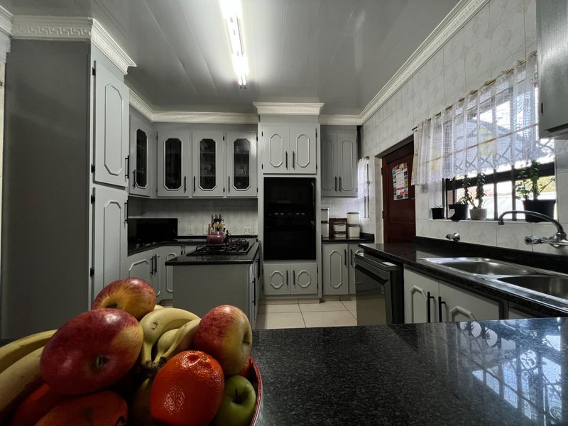 A well-maintained kitchen featuring grey cabinetry, granite countertops, a gas hob, and a built-in oven with classic crown molding details.