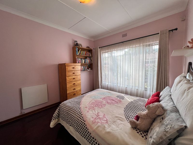 A bedroom featuring pink walls, dark wood-look flooring, a coved ceiling, and a window fitted with a security gate.