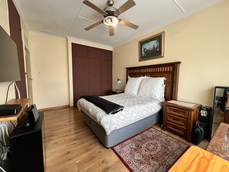 A well-proportioned bedroom featuring laminate flooring, a ceiling fan, and built-in storage cupboards.