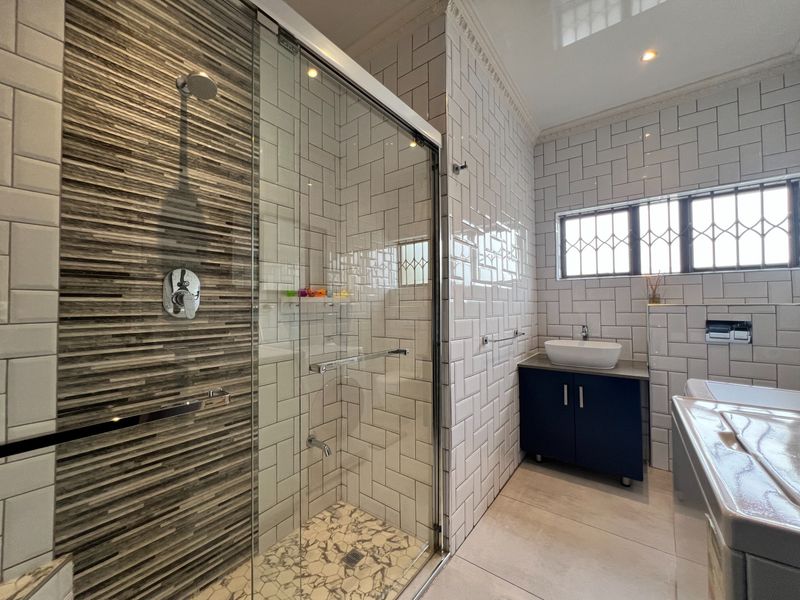Modern bathroom featuring a glass-enclosed shower with decorative accent tiling, subway wall tiles, and a sleek vanity unit with a vessel basin.
