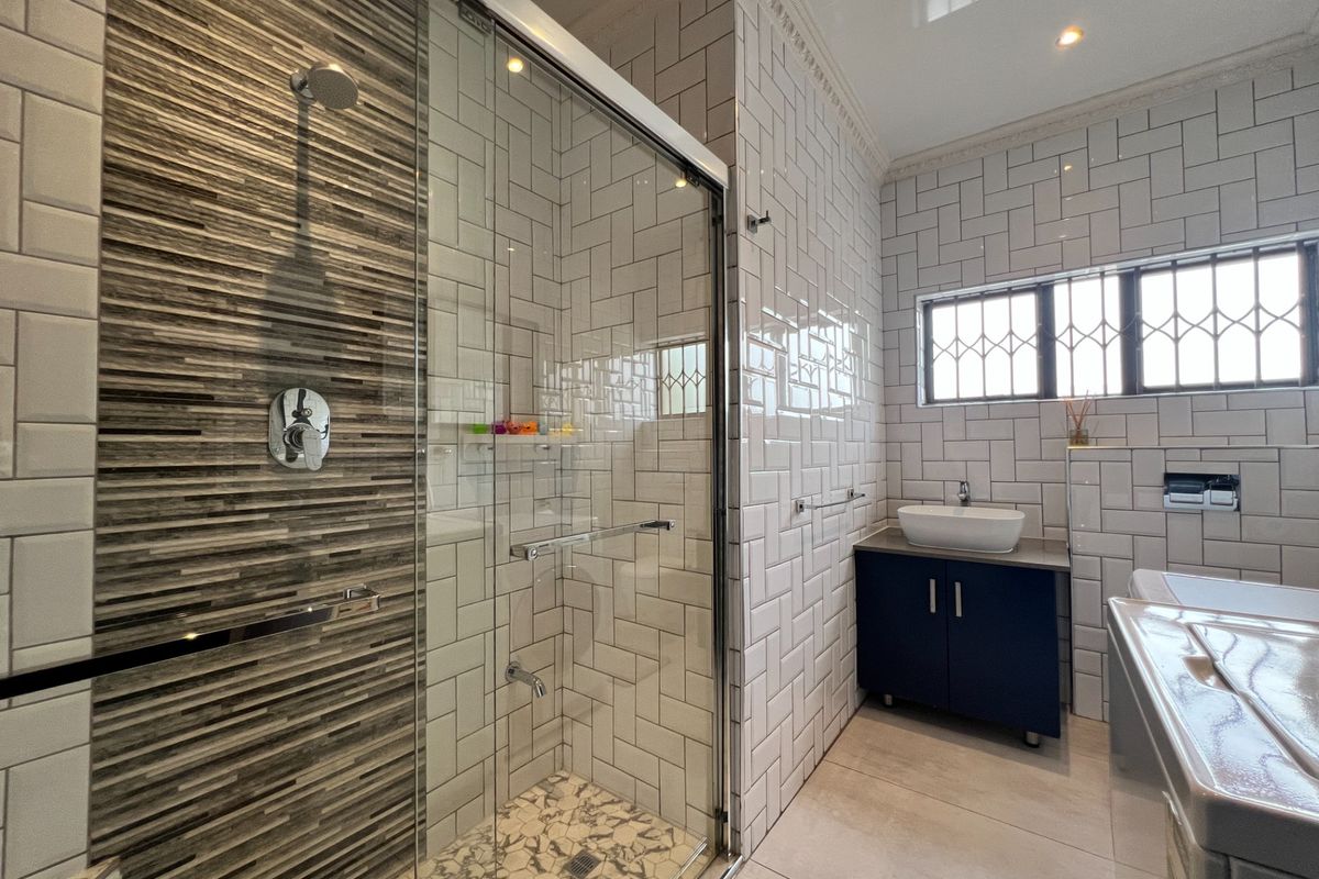 Modern bathroom featuring a glass-enclosed shower with decorative accent tiling, subway wall tiles, and a sleek vanity unit with a vessel basin.